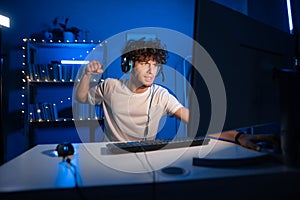 Angry arabic guy gamer showing fist and angry at losing game while playing video games at home on computer in neon light