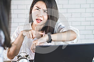 Angry Asian female boss pointing at her watch to show the time complaining her employee