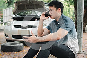 Angry Asian man and using mobile phone calling for assistance after a car breakdown on street. Concept of vehicle engine problem