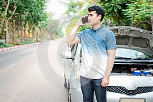 Angry Asian man and using mobile phone calling for assistance after a car breakdown on street. Concept of vehicle engine problem