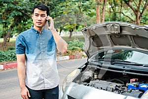 Angry Asian man and using mobile phone calling for assistance after a car breakdown on street. Concept of vehicle engine problem