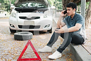 Angry Asian man and using mobile phone calling for assistance after a car breakdown on street. Concept of vehicle engine problem