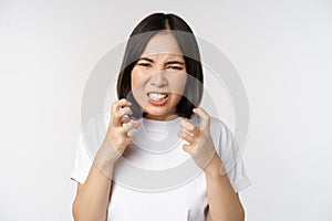 Angry asian woman cursing, looking outraged and annoyed, clench teeth and frowning furious, standing over white