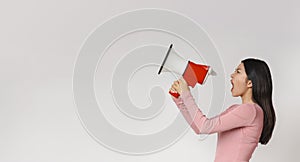 Angry asian woman shouting in megaphone over grey background