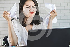 Angry Asian woman sitting at desk hand crumpling paper on table