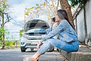 Angry Asian woman and using mobile phone calling for assistance after a car breakdown on street. Concept of vehicle engine problem