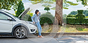 Angry Asian woman and using mobile phone calling for assistance after a car breakdown on street. Concept of vehicle engine problem