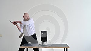Angry bald man with a red beard in the office in a business suit smashes an ax with a computer. The manager with a