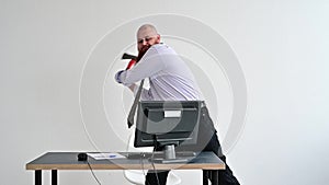 Angry bald man with a red beard in the office in a business suit smashes an ax with a computer. The manager with a