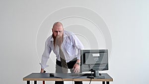 Angry bald man with a red beard in the office in a business suit smashes an ax with a computer. The manager with a