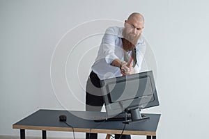 Angry bald man with a red beard in the office in a business suit smashes an ax with a computer. The manager, focused