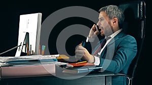 Angry bearded businessman having emotional stressful conversation on his cell phone. Black background