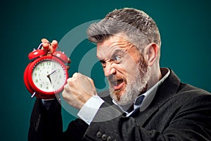 Angry bearded businessman holding alarm clock and shouting at it. Time management concept