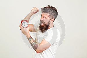 Angry bearded man breaks alarm clock. Brutal hipsater with tattoo wants to destroy clock. Time to work. Bearded manager has