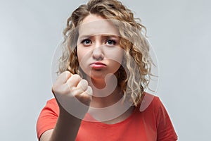 Angry blonde girl in casual t shirt raising hand furious at camera. Rage and aggressive concept