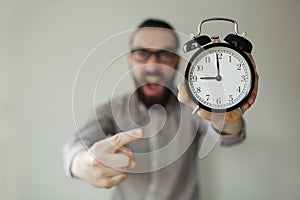 Angry boss with beard holds alarm clock screaming on camera photo