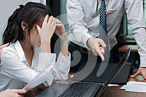 Angry boss blaming young Asian woman with hands on face in office.