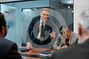 Angry boss. Furious mature businessman in formal wear shouting at his colleagues while having a meeting in the