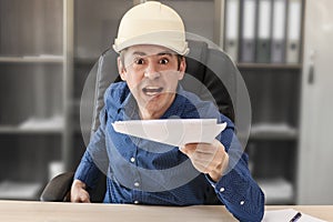 The angry boss in a helmet at his desk is holding out the cocktails. Blurred background. Builder, engineer, architect, foreman