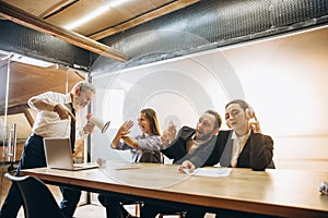 Angry boss with megaphone screaming at employees in office, scared and annoyed colleagues listening at the table