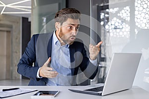 Angry boss in suit gesturing during a video call in office