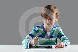 Angry boy hitting his tablet. Nervous boy studying online with laptop. Upset child has problem with gadget