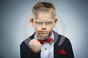 Angry boy isolated on gray background. He raised his fist to strike. Closeup