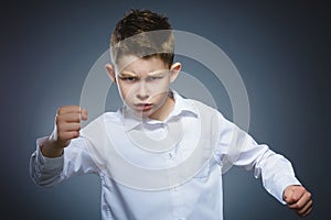 Angry boy isolated on gray background. He raised his fists to strike. Closeup