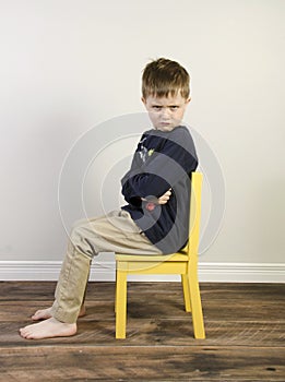 Angry boy on a yellow time out chair