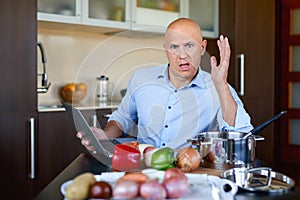 Angry brutal man in kitchen preparing food and uses laptop