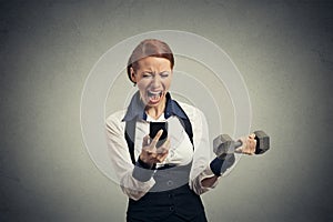 Angry business woman screaming on mobile phone lifting dumbbell