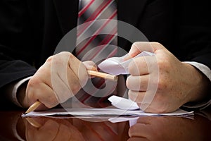 Angry businessman is breaking pencil and crumpling document