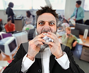 Angry businessman while eating balled paper in office.