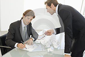 Angry Businessman With Male Colleague Writing On Paper