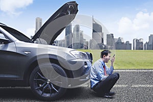 Angry businessman screams on the phone in front of breakdown car