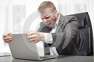 Angry businessman shaking his laptop computer