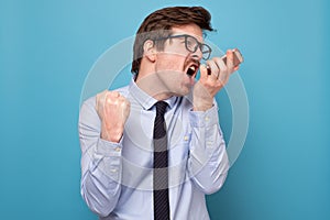 Angry businessman in shirt and tie holding mobile phone and shouting
