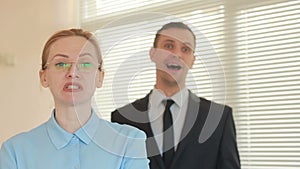 Angry businessmen, woman in the office, screaming at the camera close-up, and a subordinate behind teases her