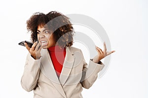 Angry businesswoman arguing on call, screaming at mobile phone speakerphone, recording voice message with furious face