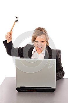 Angry businesswoman with a hammer ready to smash her laptop while sitting at office desk