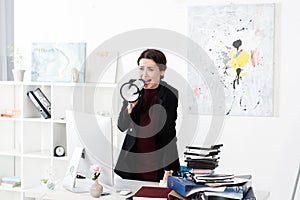 Angry businesswoman screaming in megaphone in office,