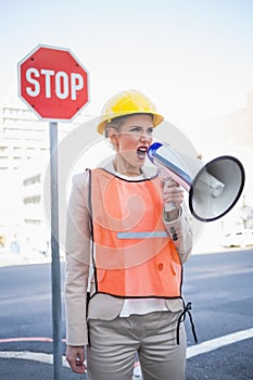 Angry businesswoman wearing builders clothes shouting in megaphone