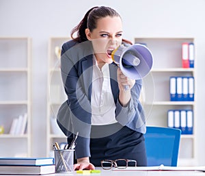 Angry businesswoman yelling with loudspeaker in office