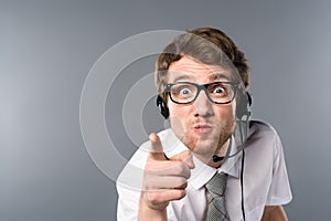 Angry call center operator in headset and glasses pointing with finger at camera.