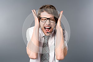 Angry call center operator in headset and glasses screaming with hands on ears.