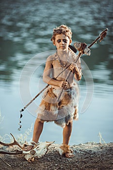 Angry caveman, manly boy with ancient primitive weapon hunting outdoors. Ancient prehistoric warrior. Heroic movie look