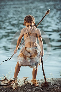 Angry caveman, manly boy with ancient primitive weapon hunting outdoors. Ancient prehistoric warrior. Heroic movie look