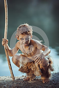 Angry caveman, manly boy with staff hunting outdoors. Ancient warrior