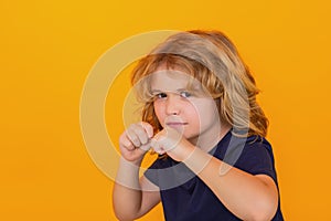 Angry child with fist gesture fight, hit on yellow studio isolated background. Kid boy with mad expression handed punch