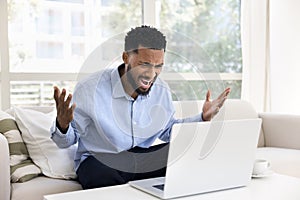 Angry concerned young African business man shouting at laptop